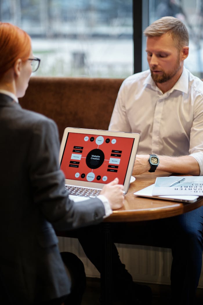 A professional man and woman discussing business strategies using laptops in an indoor setting.